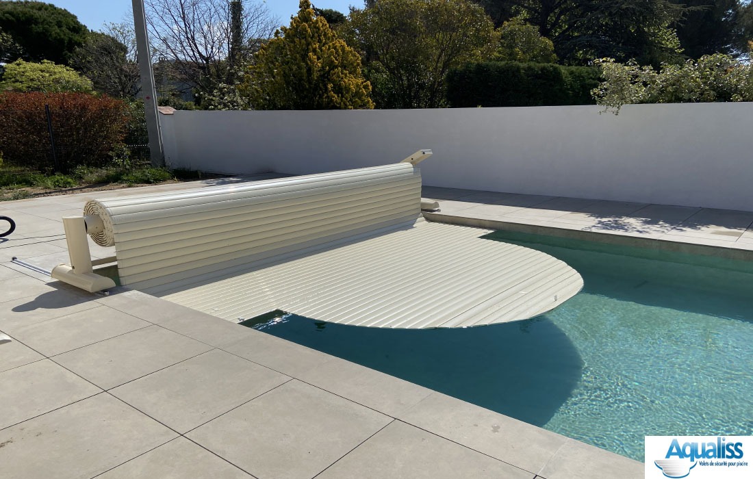 Volet de piscine mobile couleur vanille, se déroulant avec son tablier de lames sur la piscine, photographié en pleine journée.