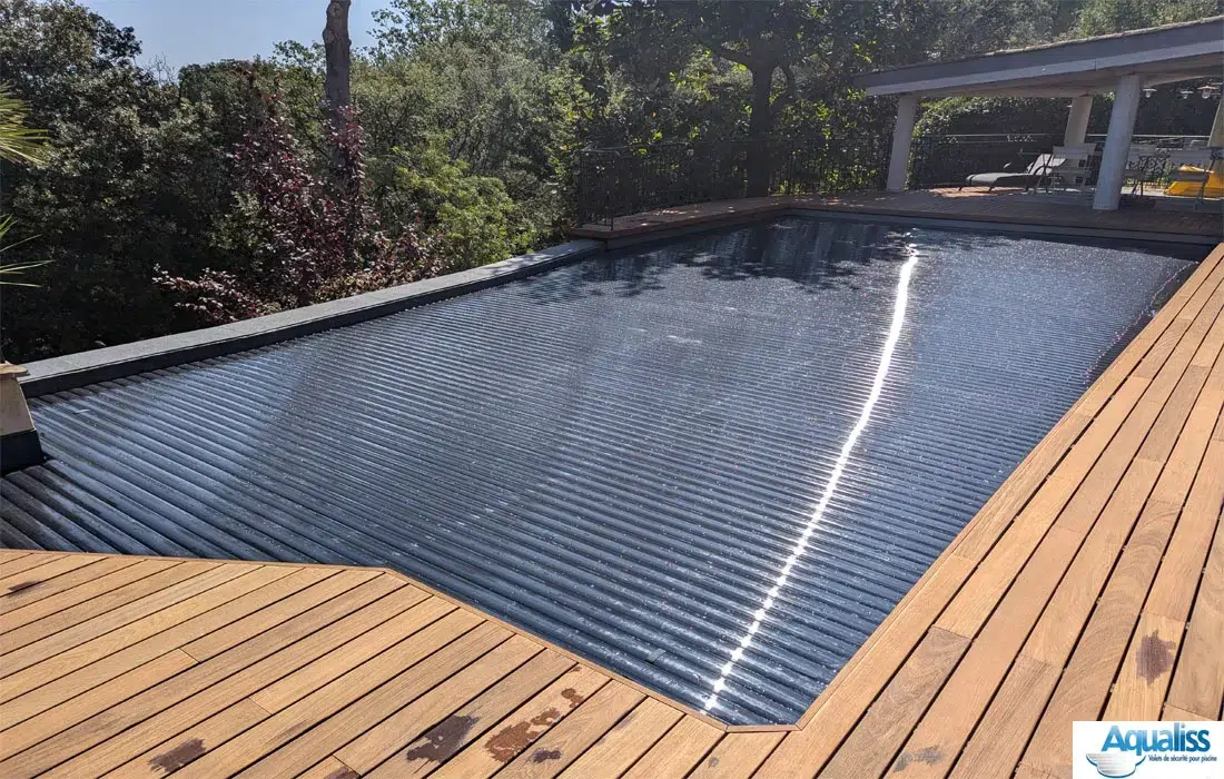 Volet immergé de piscine avec lames en polycarbonate noires, fermé sur le bassin en journée, situé en Occitanie.